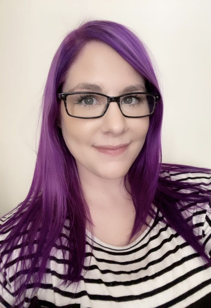 Headshot of Amanda Horn. She has long purple hair and is wearing black-framed glasses and a black and white striped shirt.