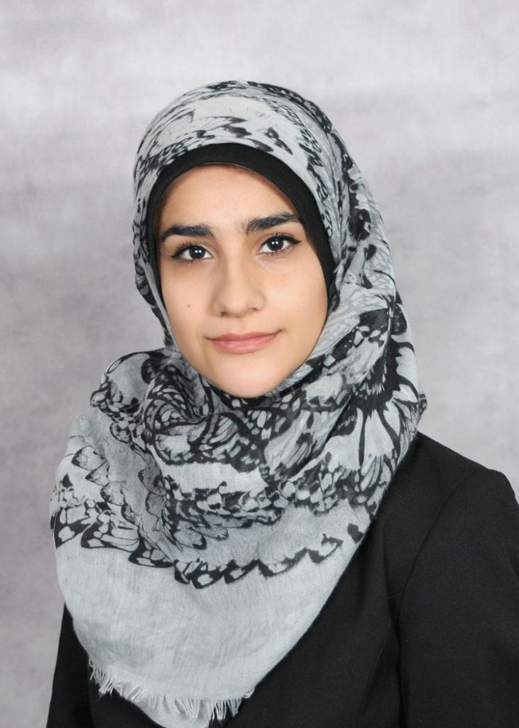 Headshot of Fatima Albrehi, wearing a gray and black patterned hijab and a black shirt.